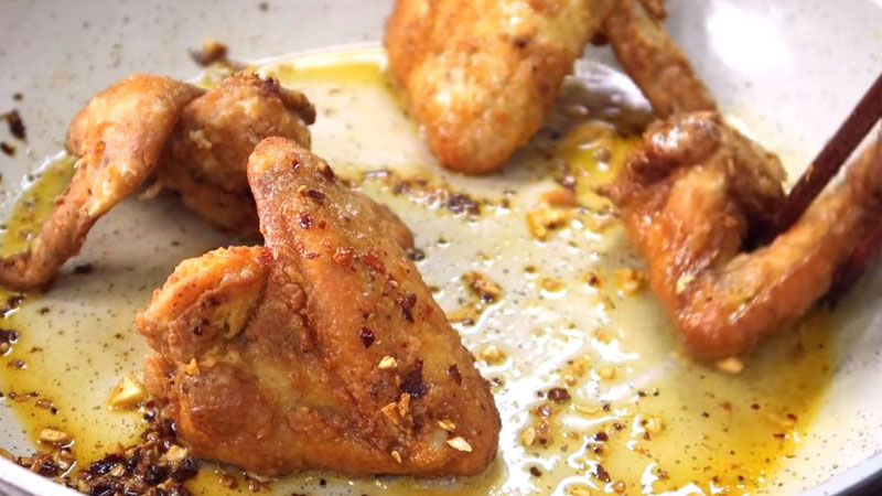 Sau đó cho cánh gà đã chiên vào, lăn đều trên chảo bơ ở lửa nhỏ để cánh gà thấm đều bơ, nhưng vẫn giữ được độ giòn ngon, rồi tắt bếp.